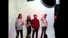 four men standing in front of a white backdrop with guitars and microphones around them