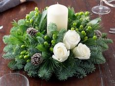 a centerpiece with white flowers, greenery and a candle on a wooden table