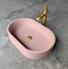 a pink sink sitting on top of a floor next to a golden faucet