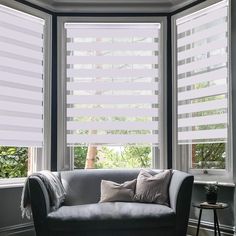 a couch sitting in front of two windows with white blinds on the top and bottom