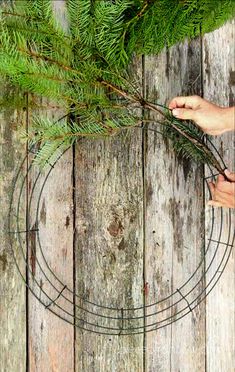 someone is holding branches in front of a wire wreath on a wooden surface with wood planks