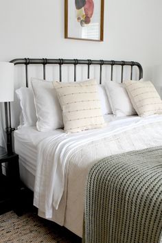 a bed with white linens and pillows in a small room next to a painting on the wall