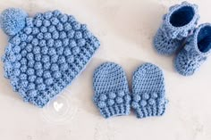 a blue crocheted hat, mittens and booties on a white surface