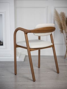 a wooden chair with white upholstered seat and backrest, in front of a plant