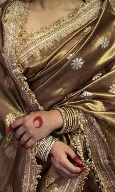 a woman in a gold sari with red nail polish on her hand and arm