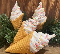 three ice cream cones with sprinkles on them sitting next to pine branches