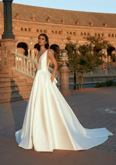 a woman in a white wedding dress standing on a brick walkway with her hands on her hips