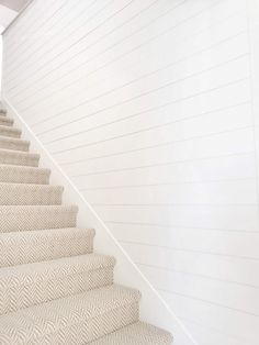 the stairs are lined with herringbone carpet and white painted walls, along with wood flooring