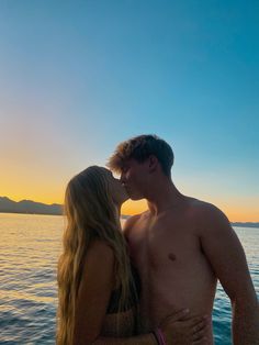 a man and woman kissing in front of the ocean at sunset on a boat with mountains in the background