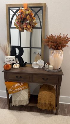 a wooden table topped with a mirror next to a vase filled with flowers and pumpkins