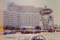 an old photo of cars and buses in front of a building with a large sign