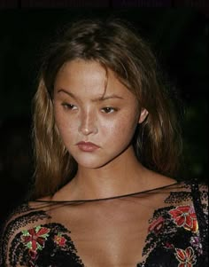 a woman in a black dress holding a cell phone and looking at the camera with an intense look on her face