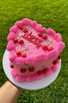 a pink heart shaped cake with strawberries on top is being held by a person