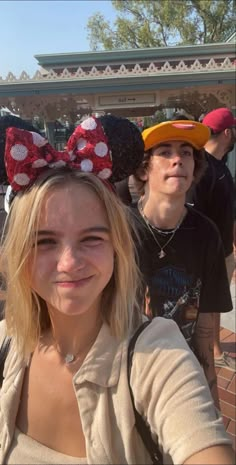 two people wearing minnie mouse ears in front of a building with other people behind them