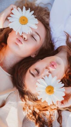 two young women laying on top of each other with white daisies in their hair