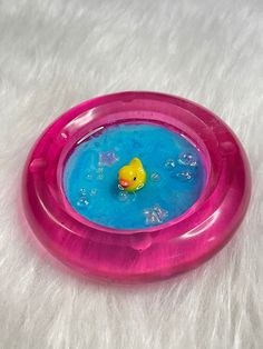 a toy rubber duck floating in a blue and pink bowl on a white fur surface