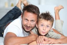 a man laying on top of a bed next to a boy with his arm around him