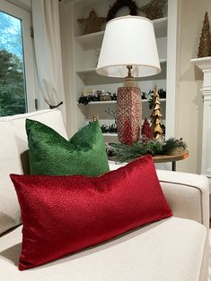 two red and green pillows sitting on top of a white couch next to a lamp