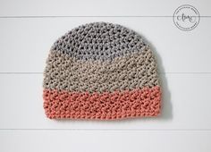 a crocheted hat with pink, grey and white stripes sits on a wooden surface