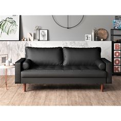 a black leather couch sitting on top of a wooden floor next to a white wall