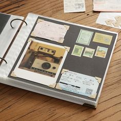 an open book on a wooden table with stamps and other items around it, including a camera