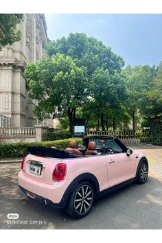 a pink convertible car parked in front of a tall building with trees on both sides