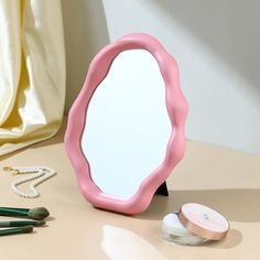 a pink mirror sitting on top of a table next to makeup