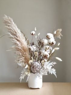 a vase filled with lots of white flowers and dry grass on top of a table