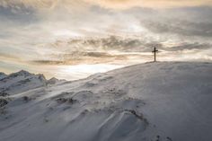 a person standing on top of a snow covered mountain with a cross in the distance