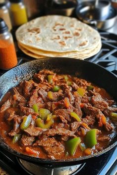 a skillet filled with beef and peppers next to tortillas