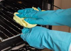 someone in blue gloves cleaning an oven with a yellow cloth on the front and bottom rack