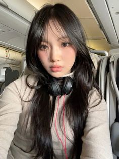 a woman with headphones on sitting in an airplane looking at the camera while listening to music