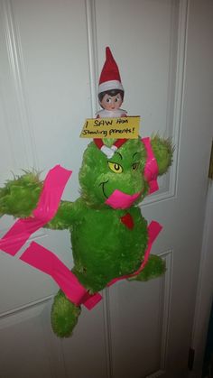 a green teddy bear with a sign on it's head sitting in front of a door