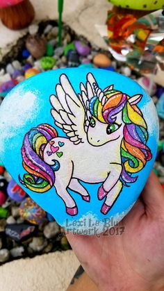 a hand holding a painted rock with a unicorn on it