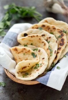 small pita breads in a basket on a table with napkins and herbs