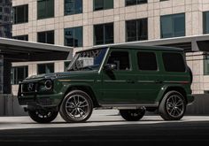 a green mercedes g - class parked in front of a building