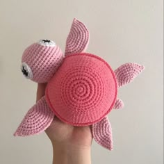 a pink crocheted turtle is held up in the air