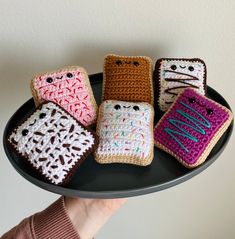 four crocheted cell phones are sitting on a black platter and one is being held by a woman