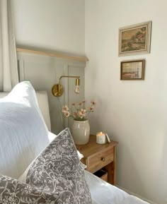 a bed with white sheets and pillows next to a wooden night stand in front of a window