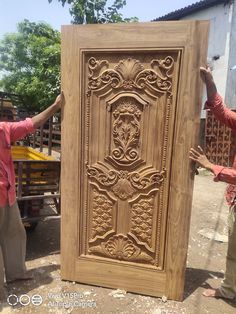 two men standing next to each other near a large wooden door with carvings on it