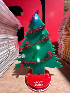 a small green christmas tree with lights on it's stand in front of a stack of books