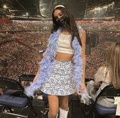 a woman wearing a blue feather jacket and skirt standing in front of a crowd at a concert