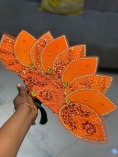 a hand holding an orange fan with beads and tassels on it's side