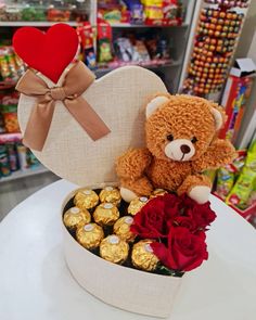 a teddy bear sitting on top of a heart shaped box filled with chocolates and roses