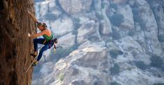 a man climbing up the side of a mountain with his hands in the air while holding onto ropes