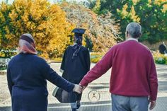 two men and a woman holding hands in front of trees with yellow leaves on them