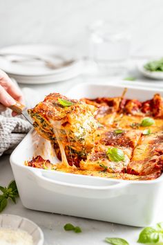 someone is taking a piece of lasagna out of the casserole dish