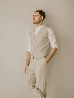 a man standing in front of a white wall with his hands on his hips wearing a vest and pants