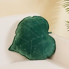 a green leaf shaped pillow sitting on top of a white couch next to a potted plant