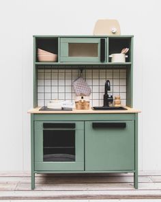 a green kitchen cabinet with dishes on top and cupboards above the sink, in front of a white wall